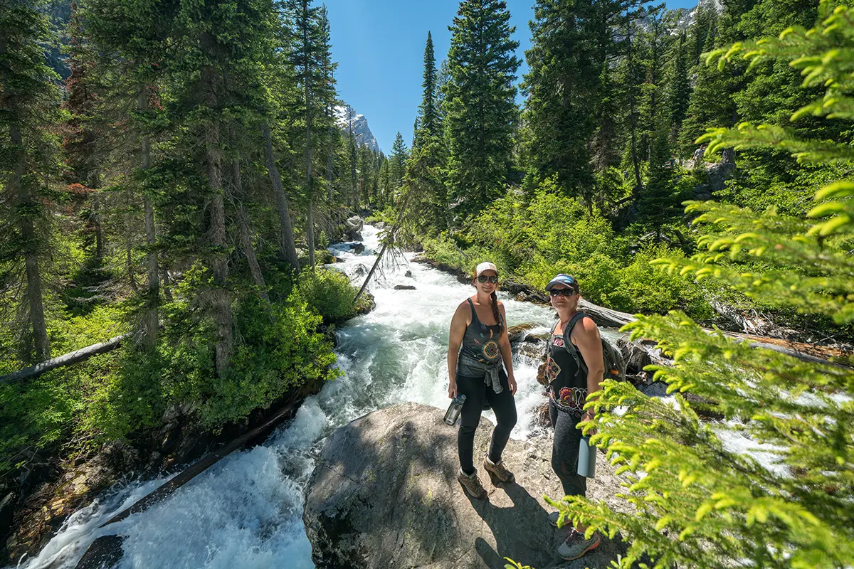 Two Women Smiling by River on Yellowstone Hiking Tour - Backcountry Safaris